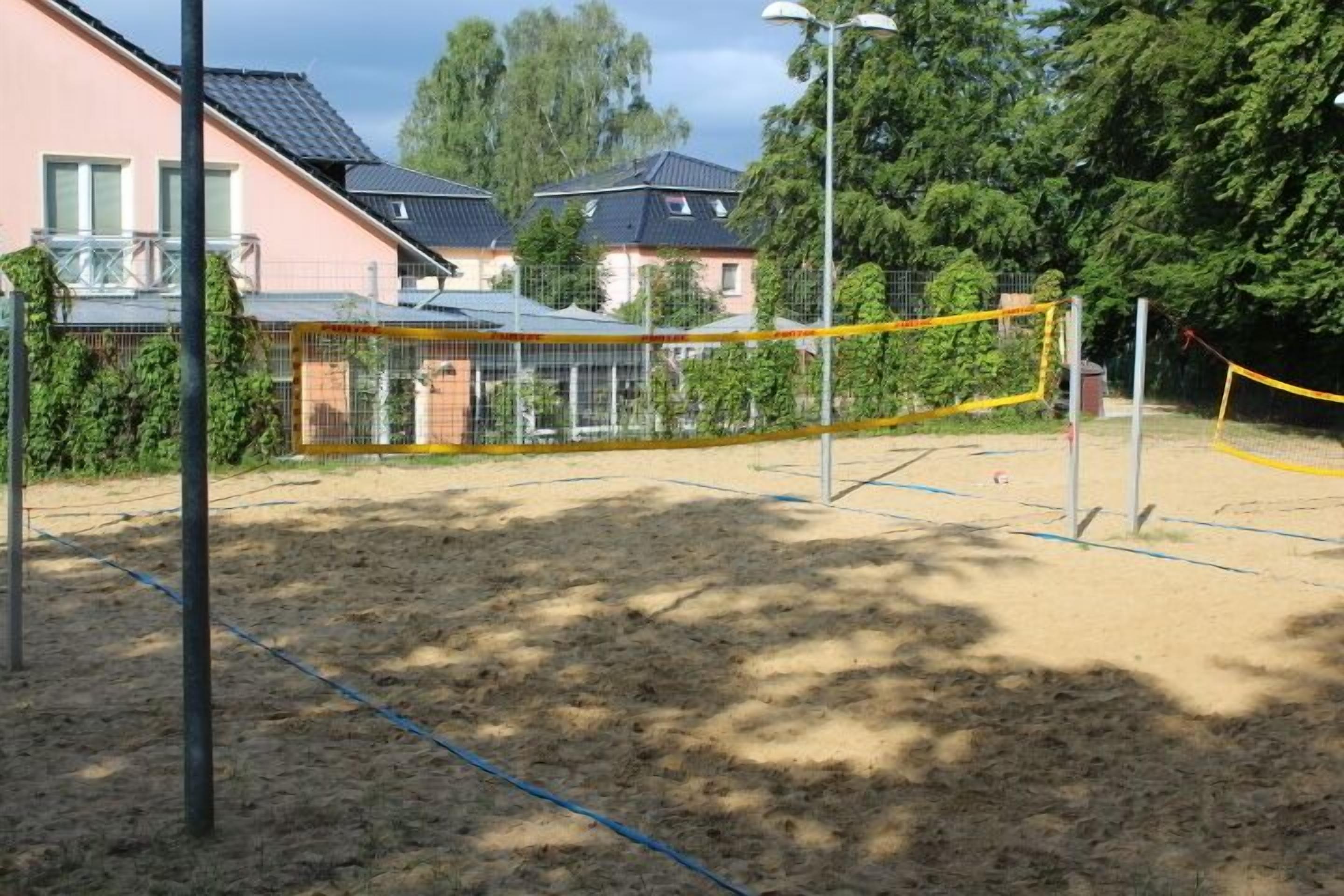 A volleyball court with a net, surrounded by a fence and trees.