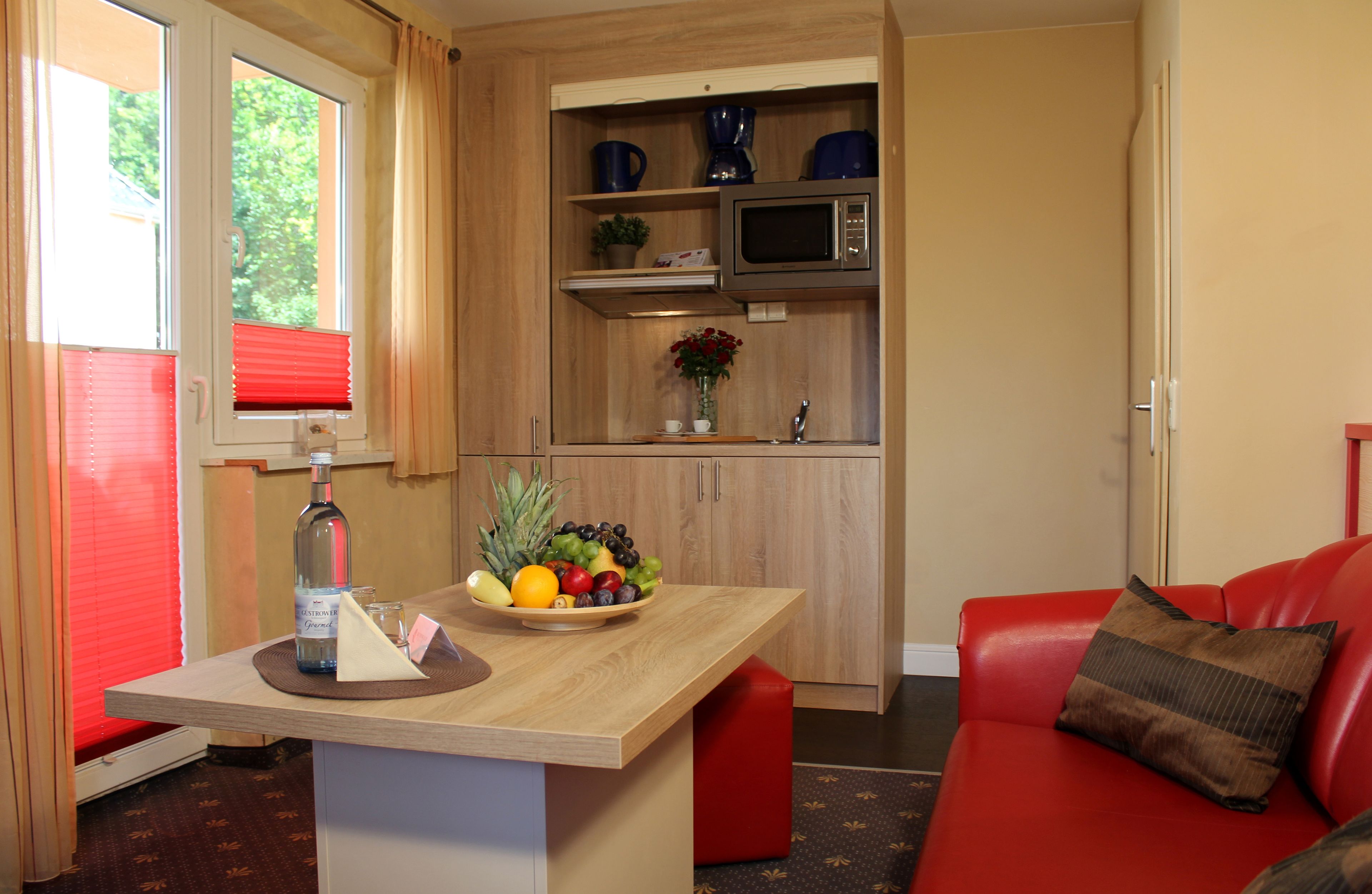 A compact kitchen with a microwave, a fruit bowl, and a bottle on the counter.