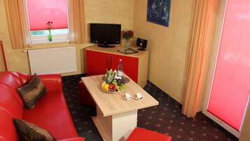A red sofa, a wooden table with a fruit bowl, a television, and a small cabinet with a vase.