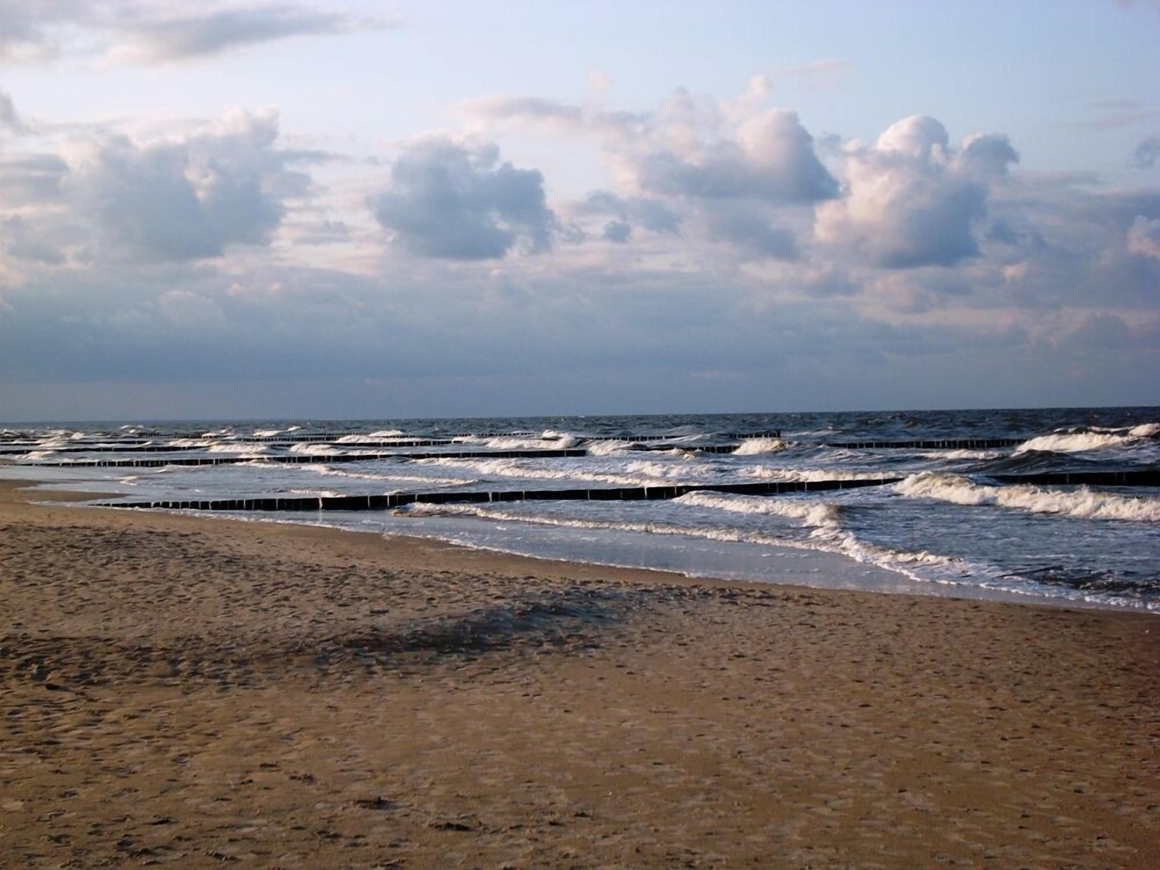 A beach with waves breaking on the shore and a cloudy sky.