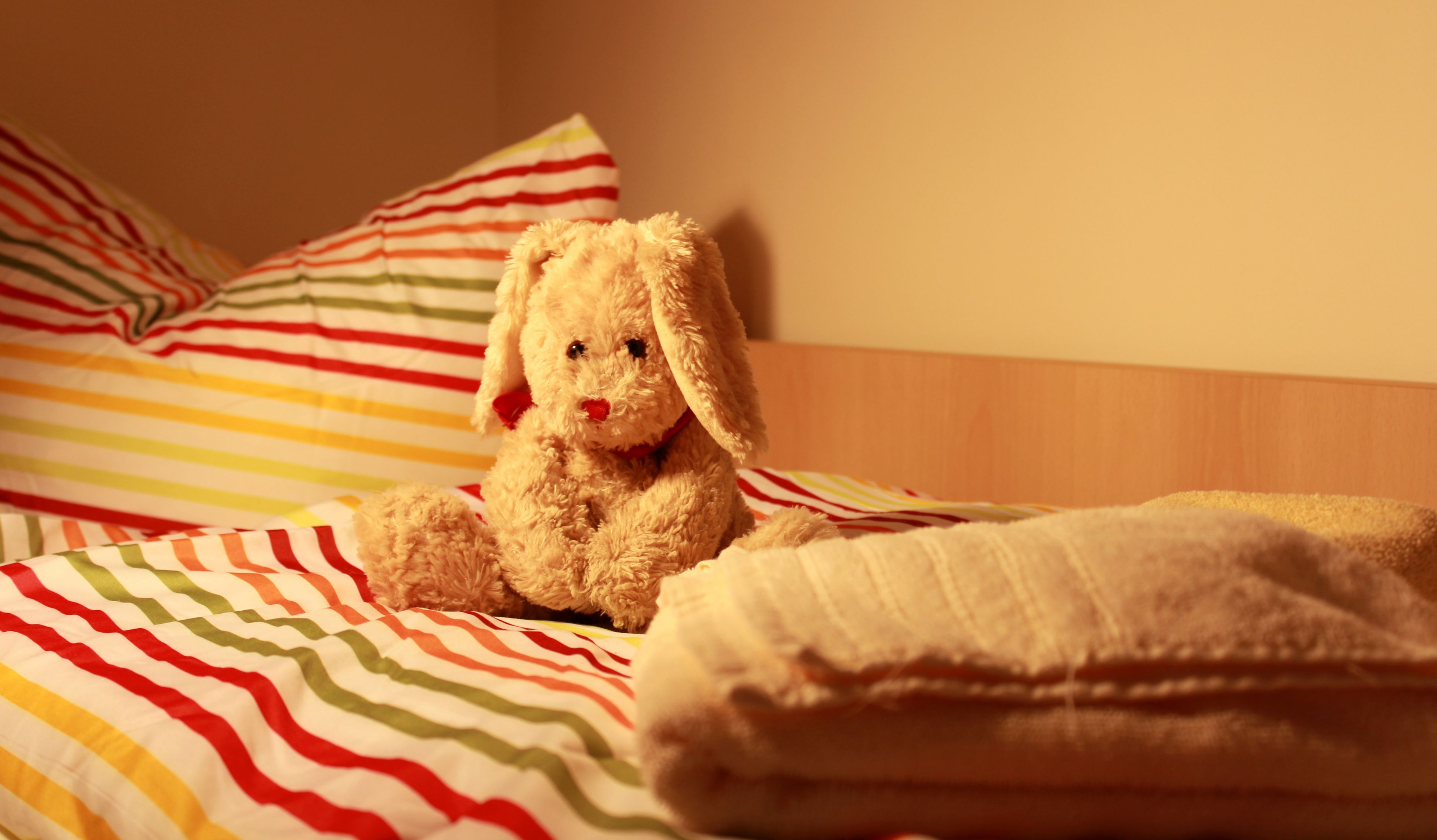 Een teddybeer zit op een bed met gestreepte kussens en een deken.