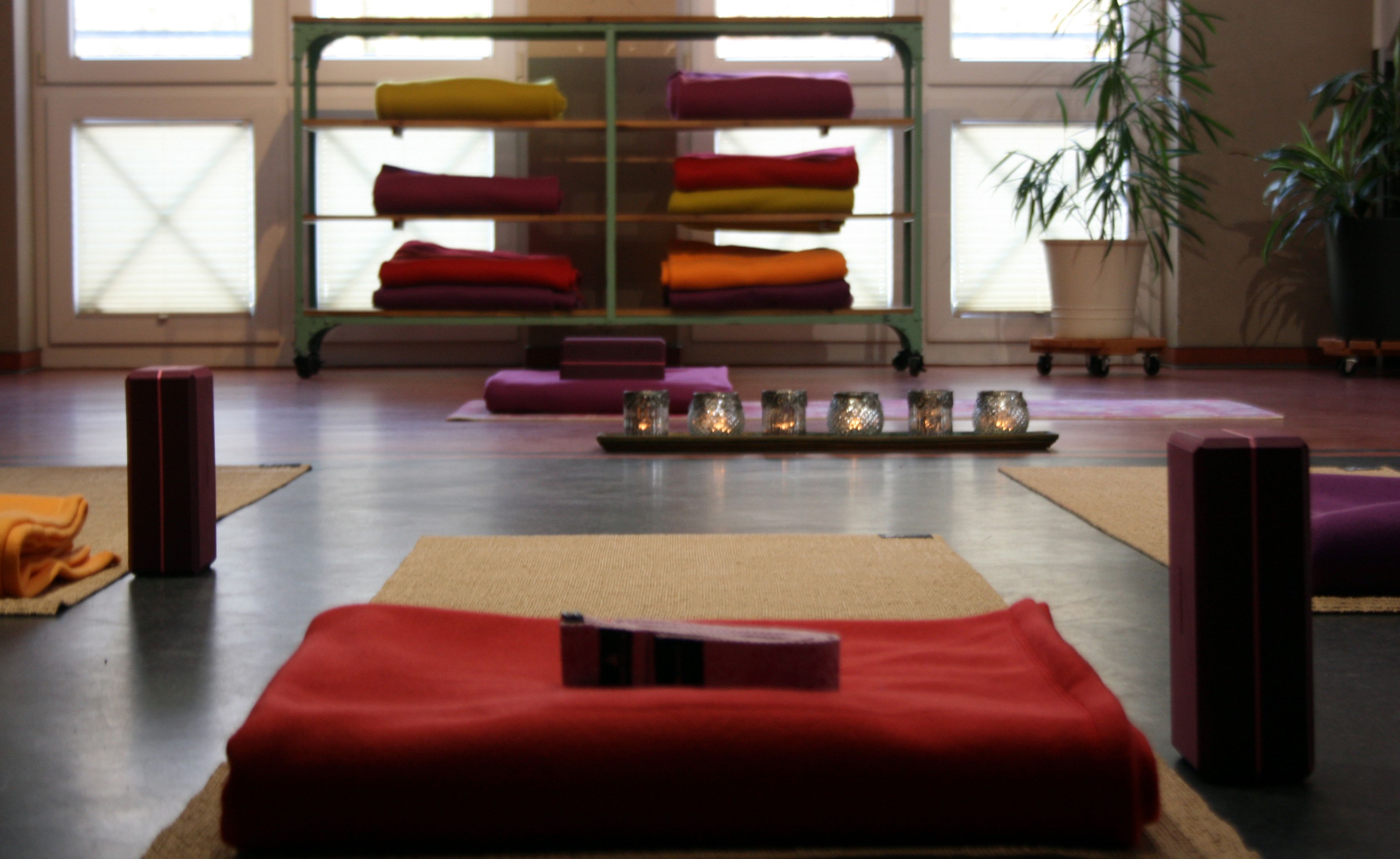 A room with a meditation area featuring a mat, cushions, and a shelf with folded blankets.