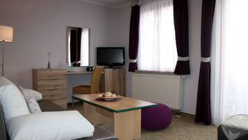 Habitación de hotel con sofá, escritorio de madera, televisor, radiador y cortinas moradas.
