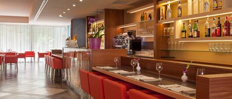 Un área de bar moderna con una barra alargada, sillas rojas y una variedad de botellas y vasos.