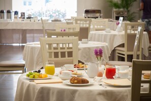 Ein Frühstücksbuffet mit gedeckten Tischen, darunter Obst, Gebäck und Getränke.