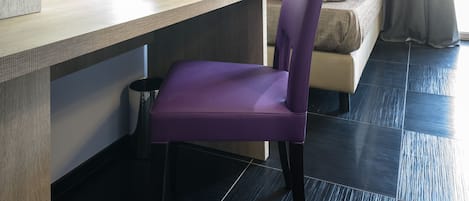 A modern hotel room with a bed, a desk with a chair, a flat-screen TV, and a small plant on the desk.