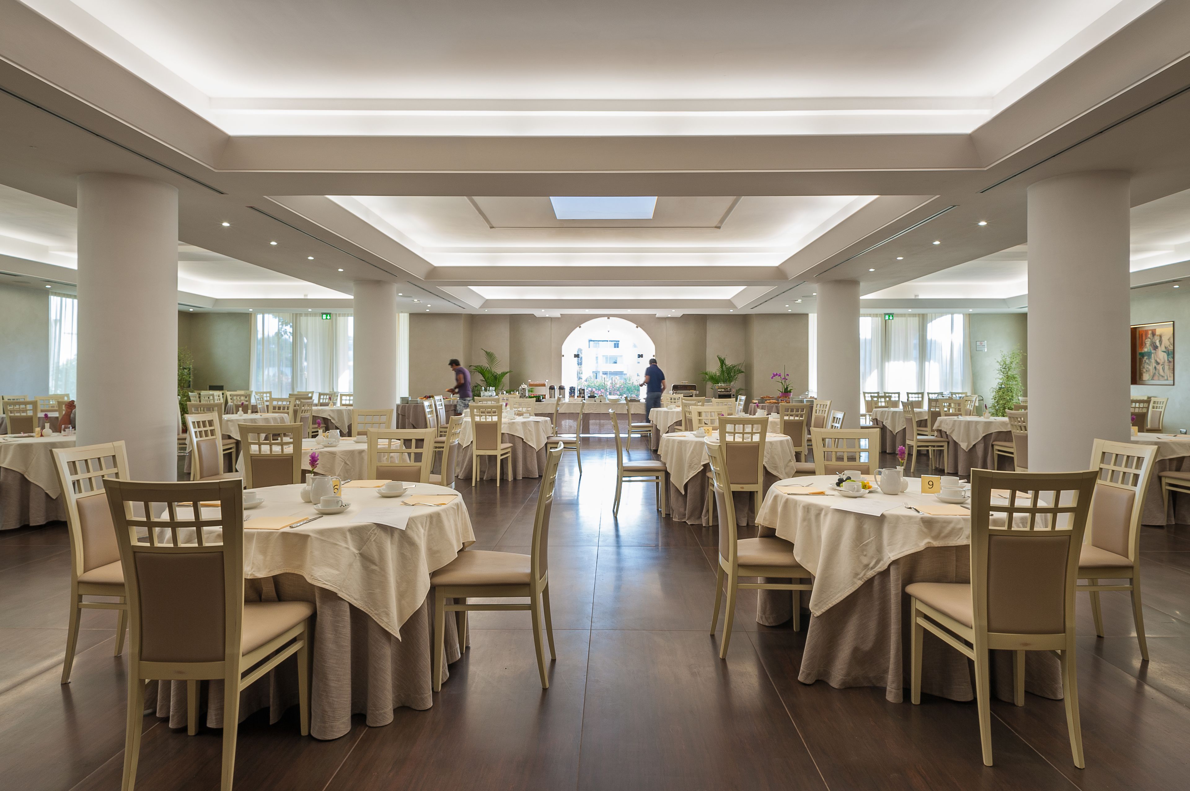 Un'ampia sala da pranzo con diversi tavoli e sedie, un arco centrale e ampie finestre.