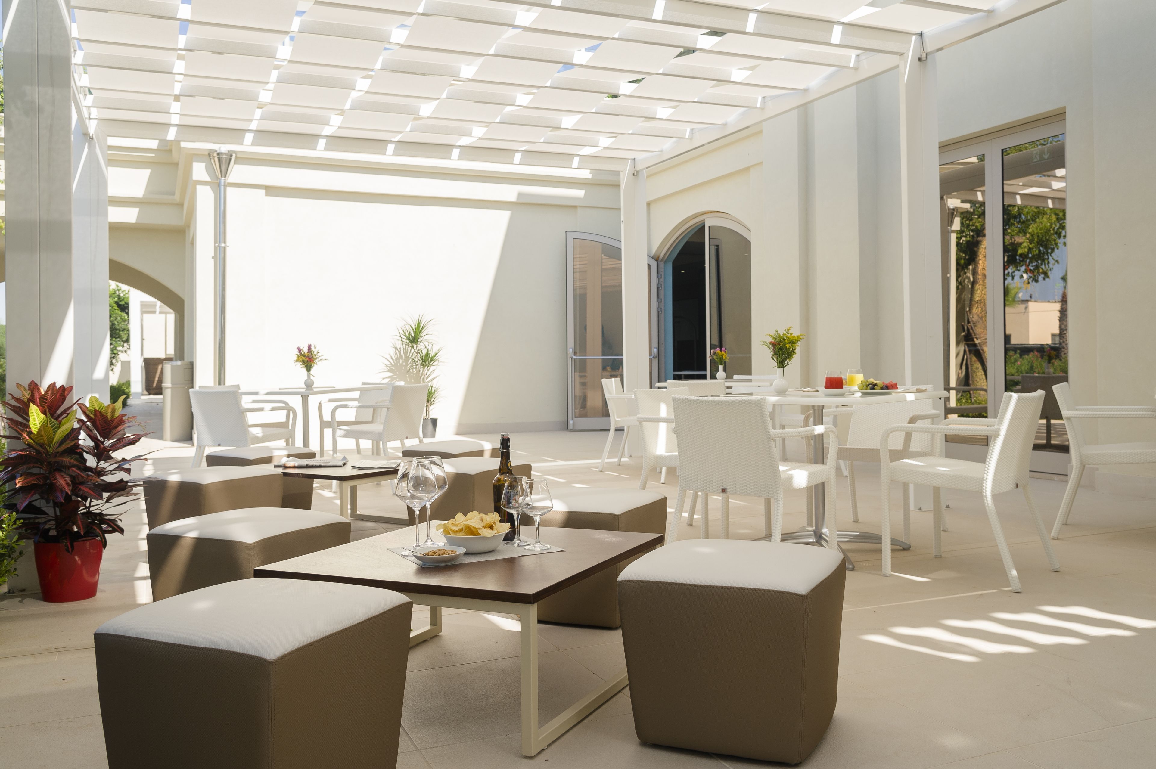 Ein Terrassenbereich im Freien mit weißer Möbel, darunter Tische und Stühle, und Kübelpflanzen.