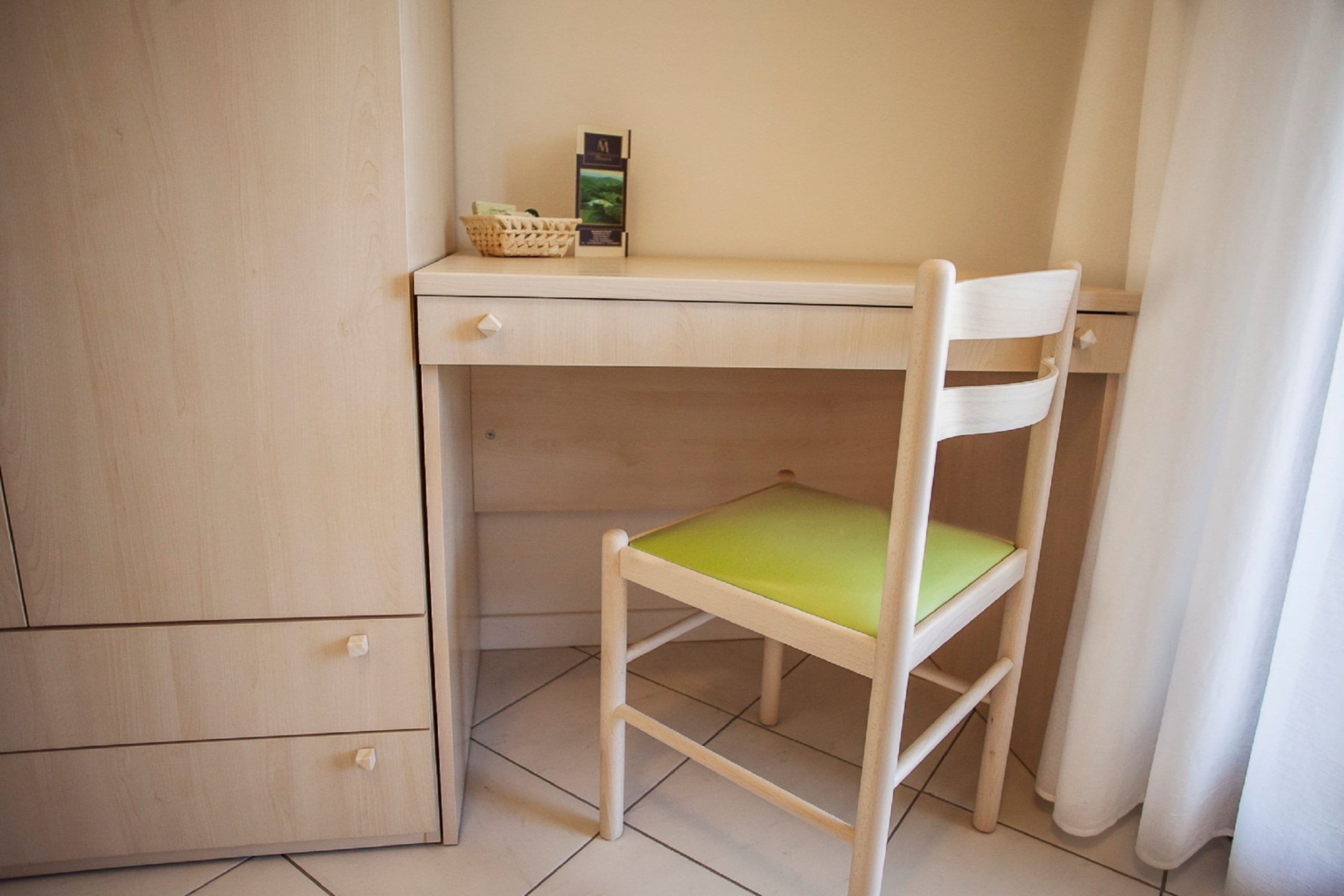 A wooden desk with a green cushioned chair, a basket, and a small item on the desk.