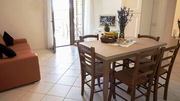 Uma área de refeições com uma mesa posta para quatro pessoas, um sofá com almofadas e uma televisão ao fundo.