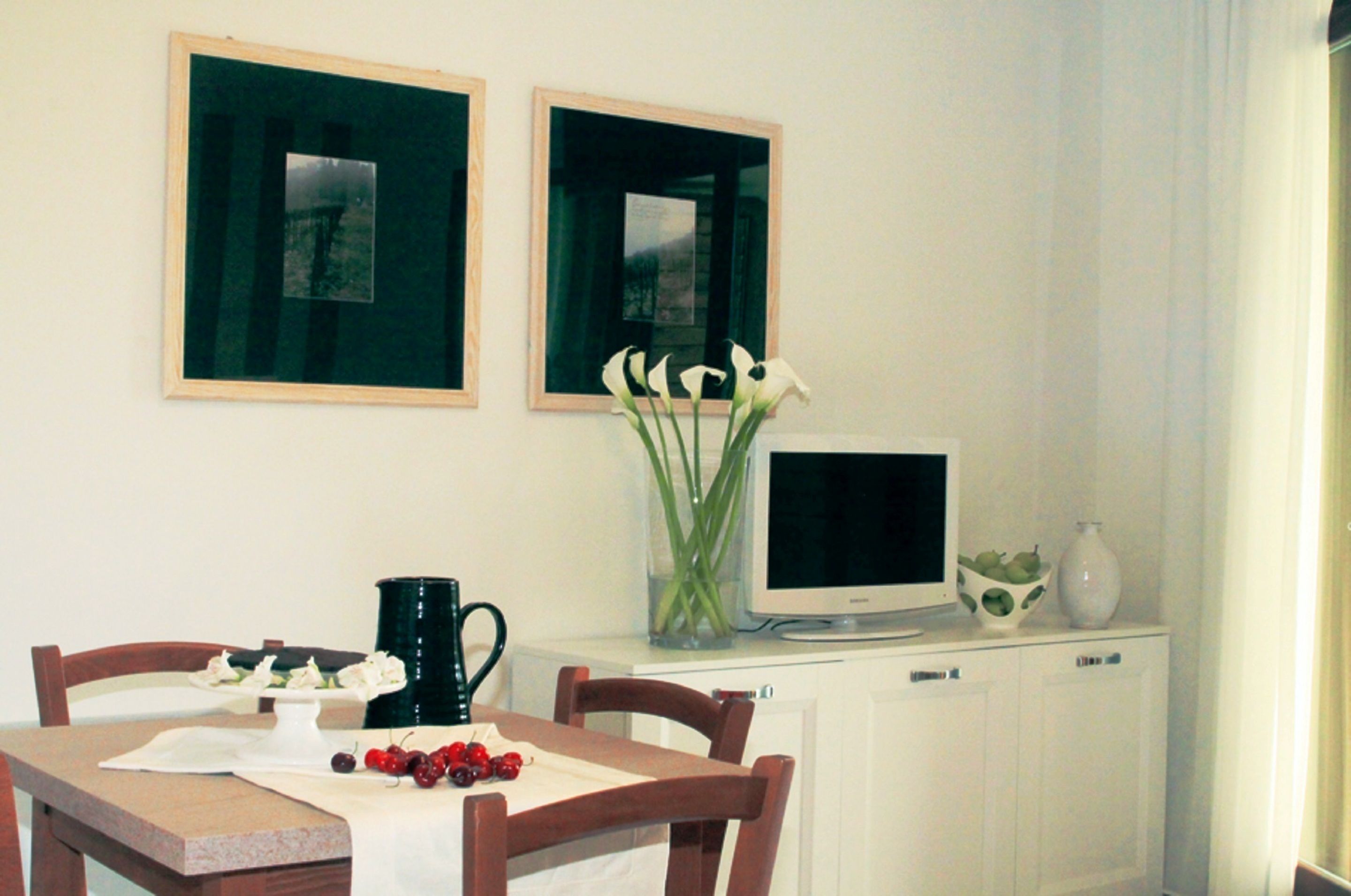 A dining area with a table set for two, a television on a cabinet, and a vase with flowers.