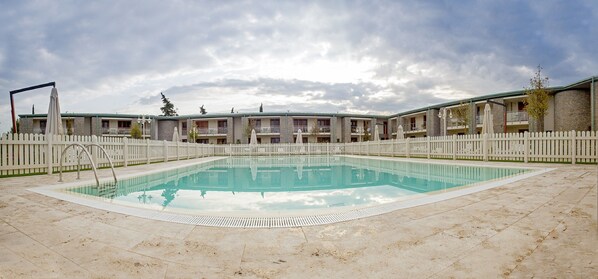 A swimming pool surrounded by a white picket fence, with a row of multi-story buildings in the background. - Chianti Village Morrocco (Barberino Tavarnelle)