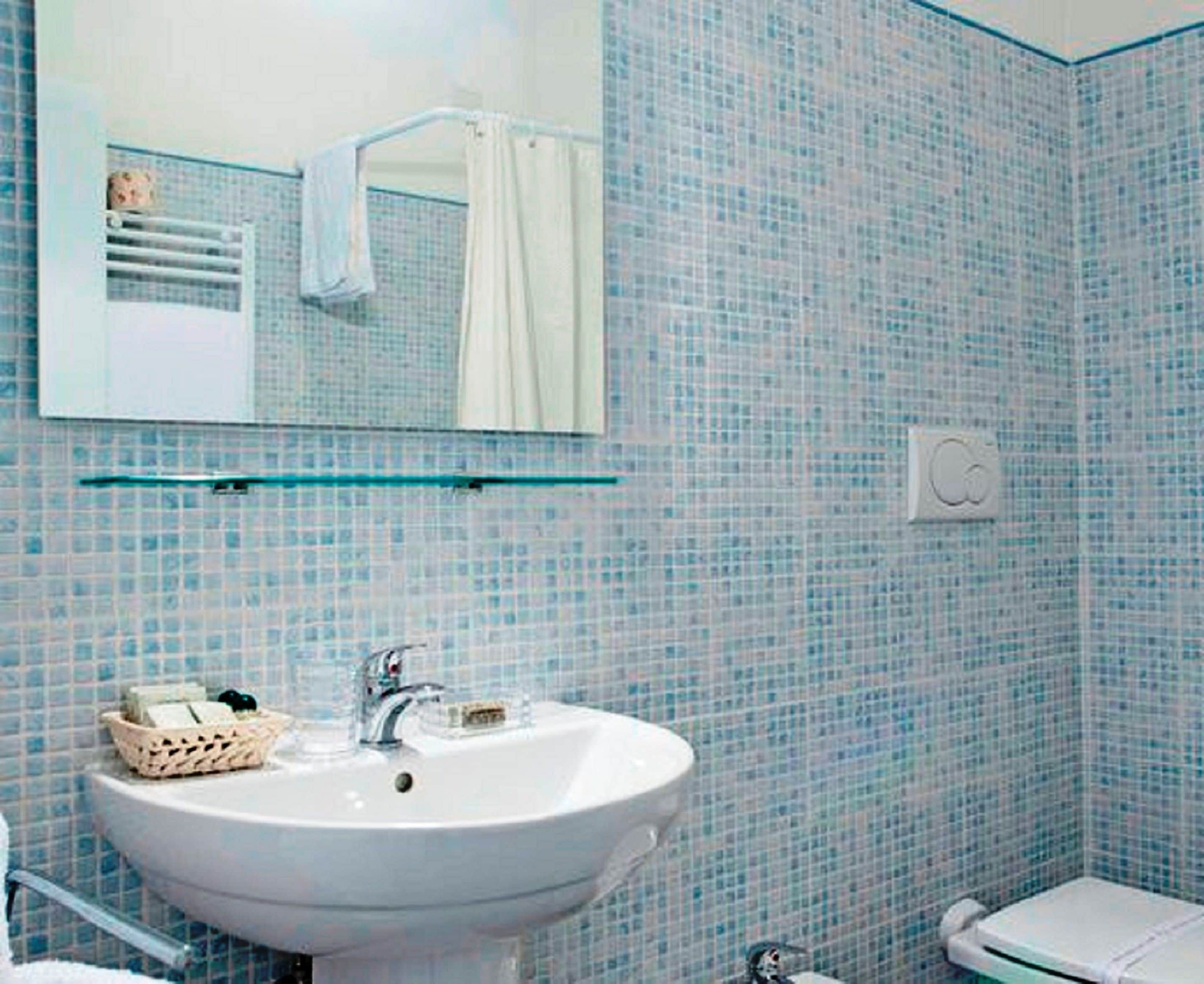 A bathroom with a white sink, a mirror, and a tiled wall.