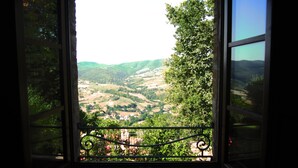 A window with a view of a valley, a balcony with a metal railing, and a clear sky.