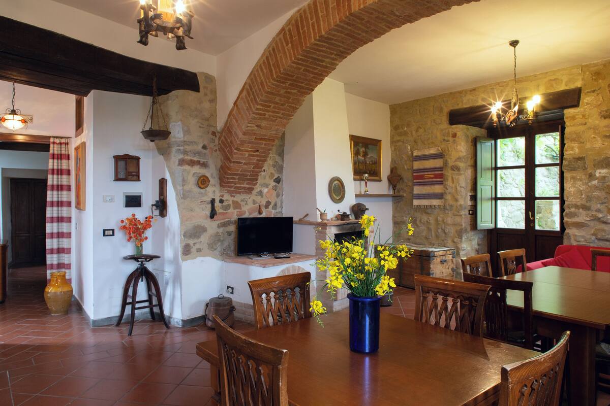 A dining area with a brick arch, wooden chairs, a table, and a vase of flowers.