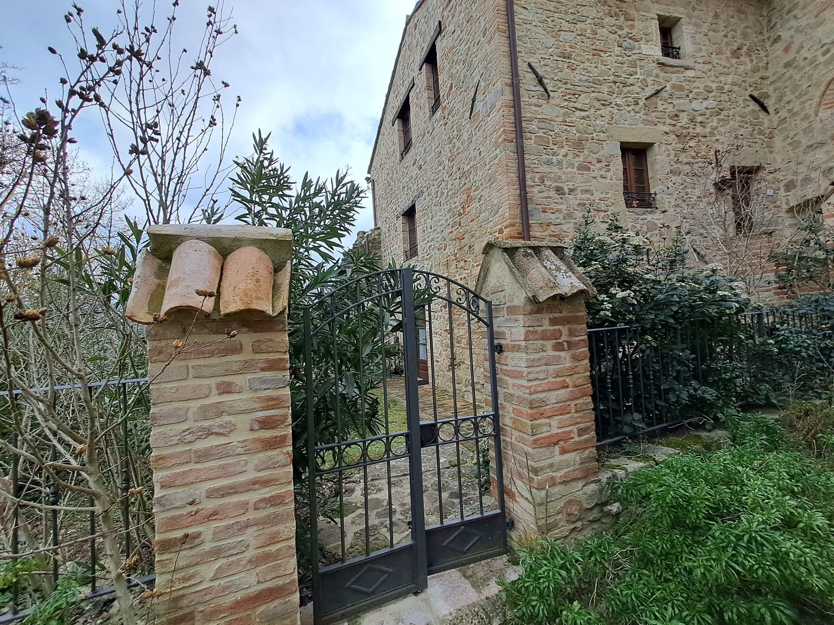 Un bâtiment en pierre doté d’un portail en métal, entouré de verdure et d’arbres.