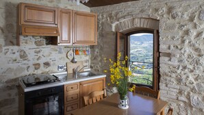 A rustic kitchen with stone walls, wooden cabinets, a stove, and a window with a view.