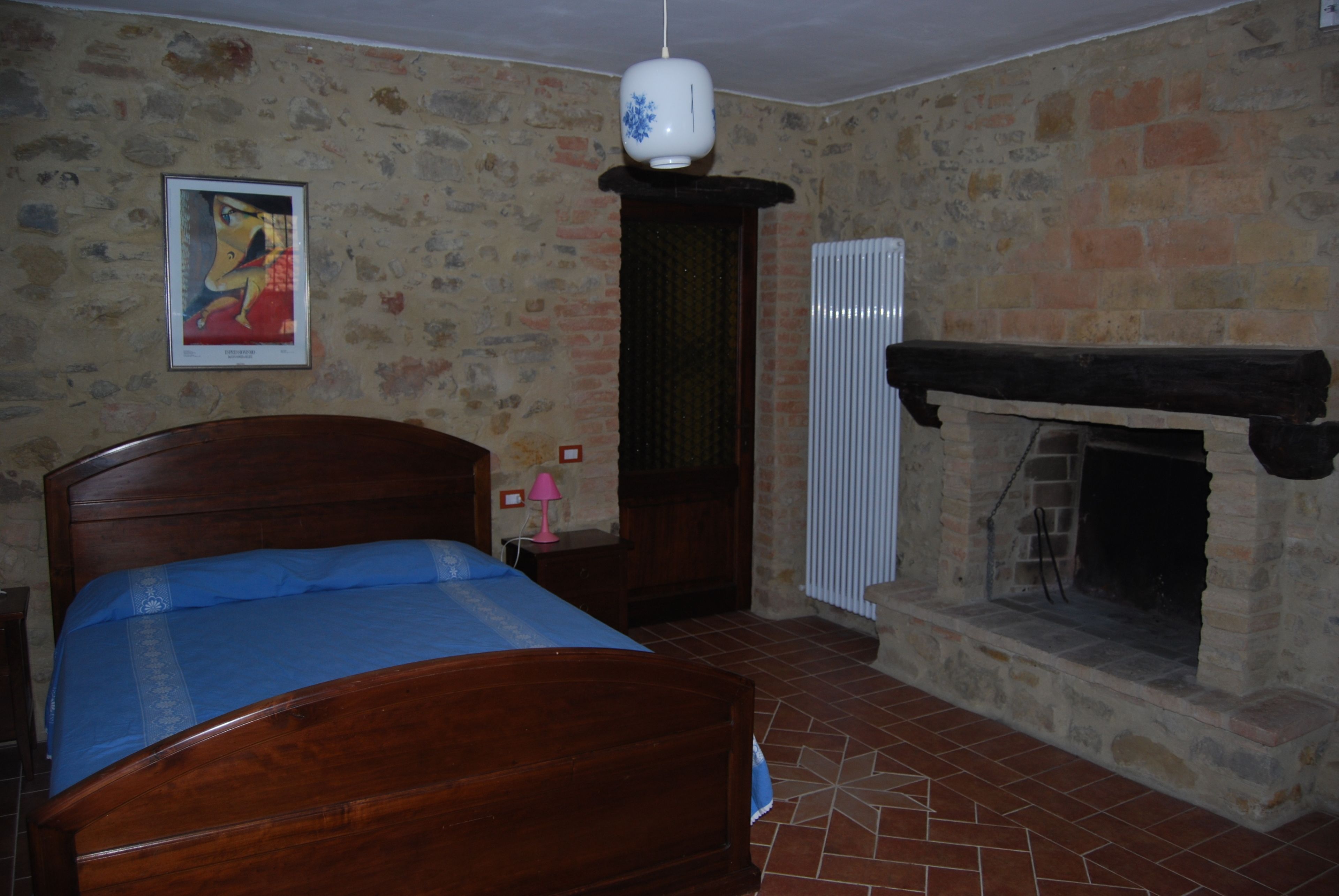 Een slaapkamer met een houten bed, een stenen openhaard en een ingelijste foto aan de muur.