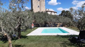 A pool area with a stone building in the background, surrounded by olive trees.