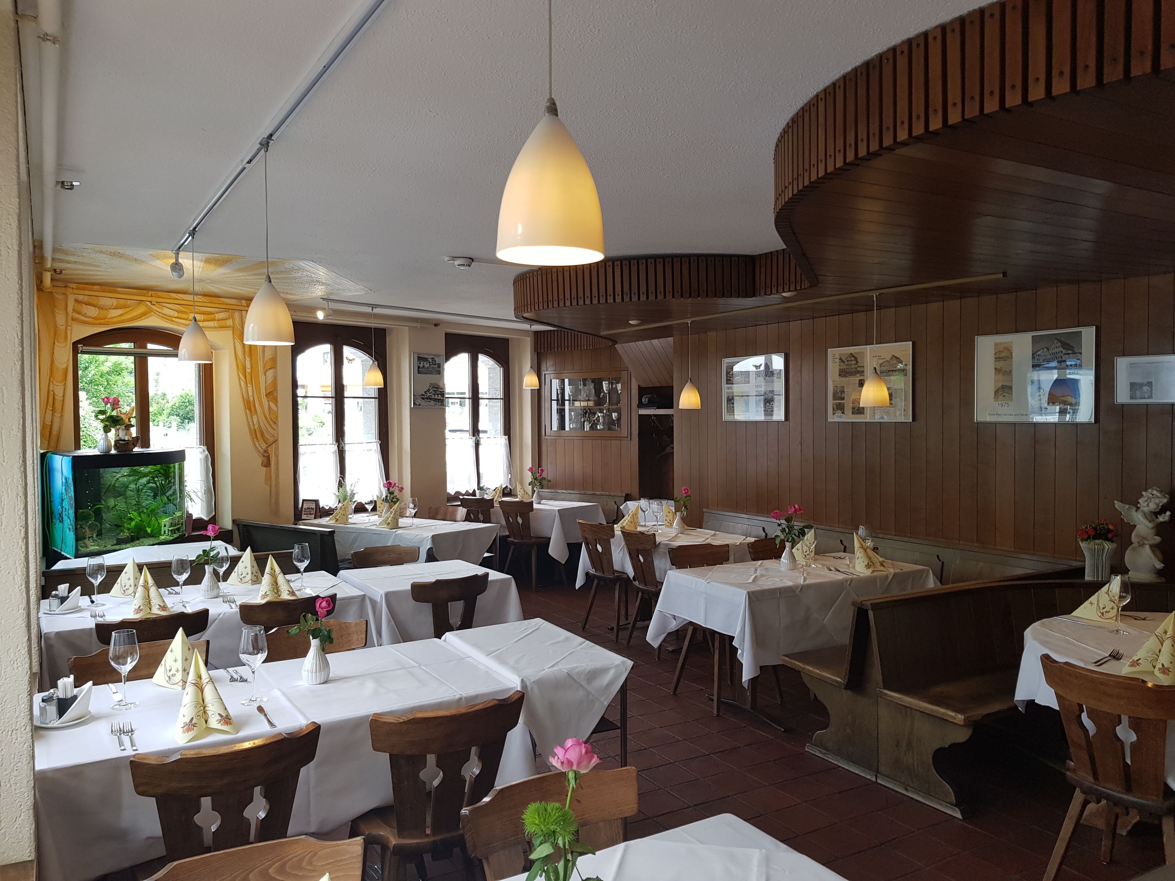 A restaurant with multiple tables, wooden paneling, and hanging pendant lights.