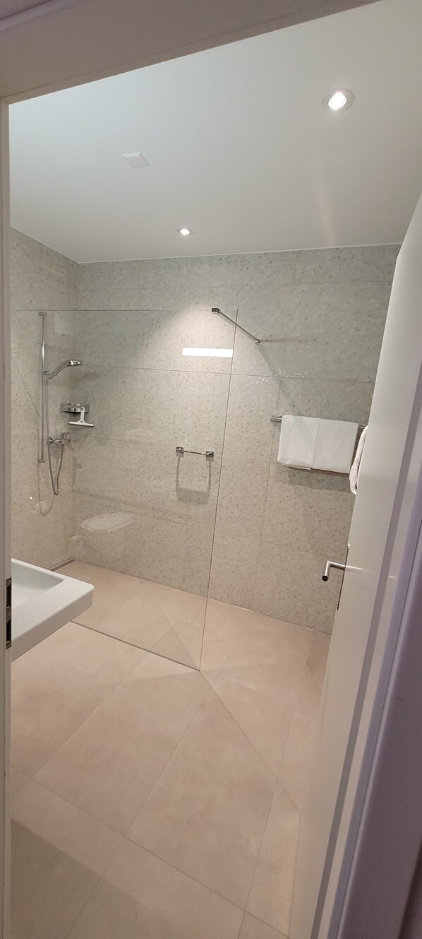 A modern bathroom with a glass-enclosed shower, a white sink, and a towel rack.