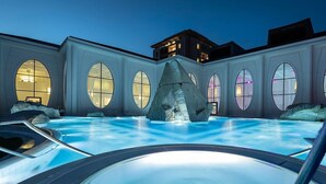 A swimming pool with a large rock centerpiece, surrounded by a building with large windows and a modern architectural design. - Hotel Post (Sargans)