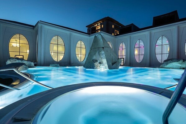 Una piscina con una gran roca como elemento central, rodeada por un edificio de grandes ventanales y diseño arquitectónico moderno.