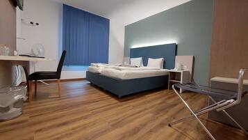 Ein Hotelzimmer mit einem Bett, einem Schreibtisch mit Stuhl, einer Schreibtischlampe und einem Fenster mit Vorhängen.