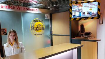 Een receptiebalie met het logo van Hotel Post, een telefoon en een televisiescherm waarop een ontbijtbuffet wordt getoond.