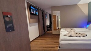 A hotel room with a wooden floor, a bed with a white comforter, a TV mounted on the wall, and a small desk with a chair. - Hotel Post (Sargans)