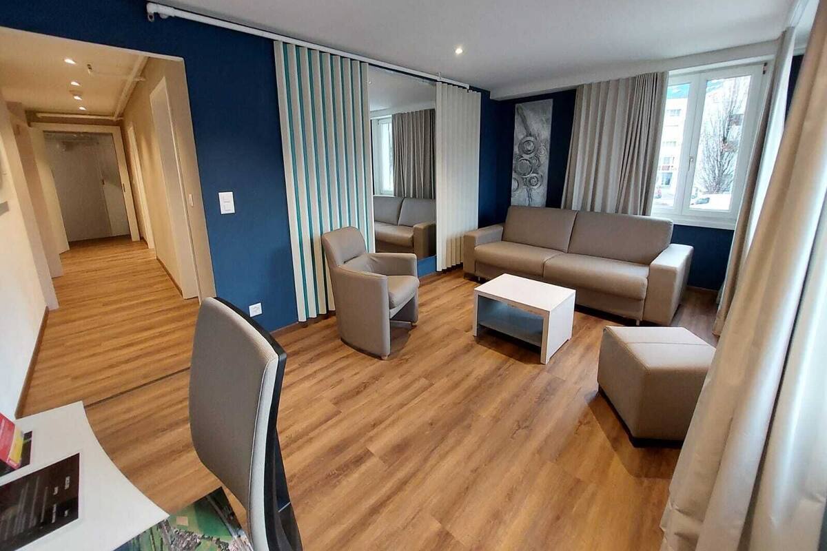 A modern living room with a sofa, armchairs, and a coffee table. There is a hallway leading to another room.