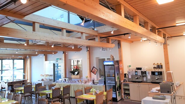 A restaurant with wooden beams, tables with yellow tablecloths, and a refrigerator with a beer logo. - Hotel Post (Sargans)