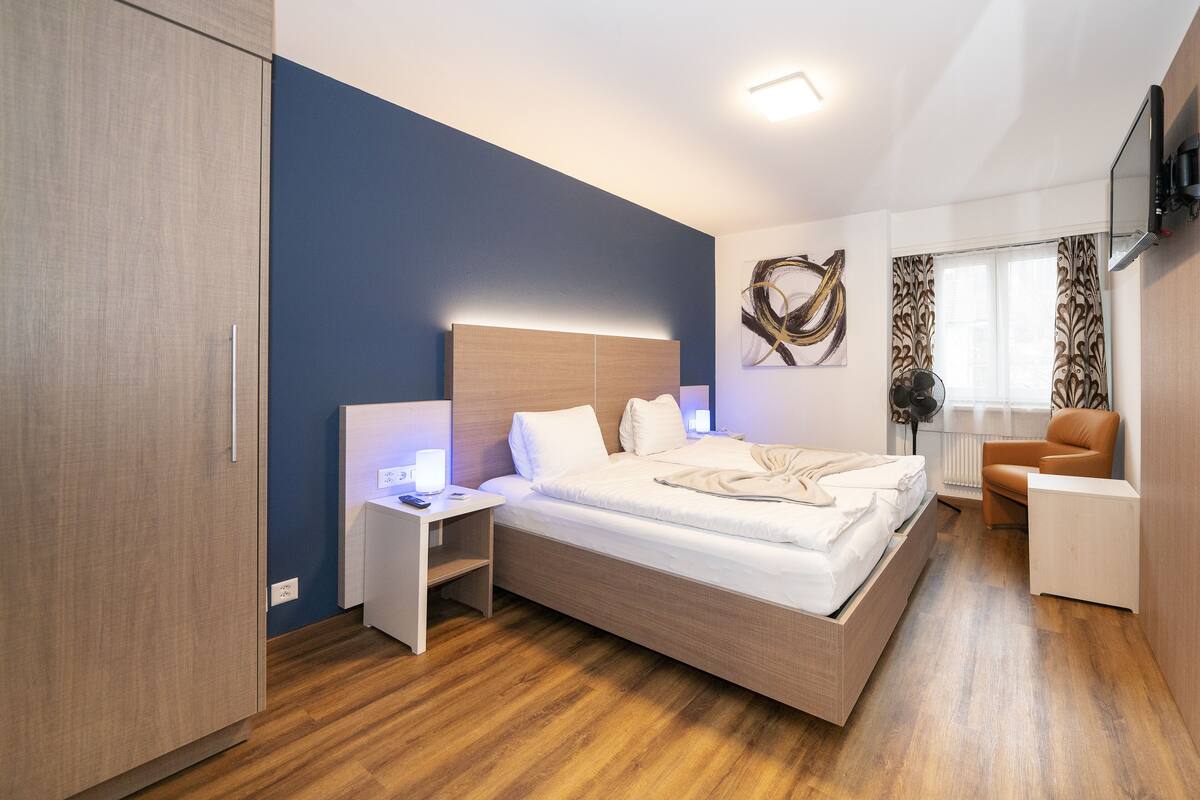 A modern bedroom with a bed, bedside tables, a chair, and a TV.