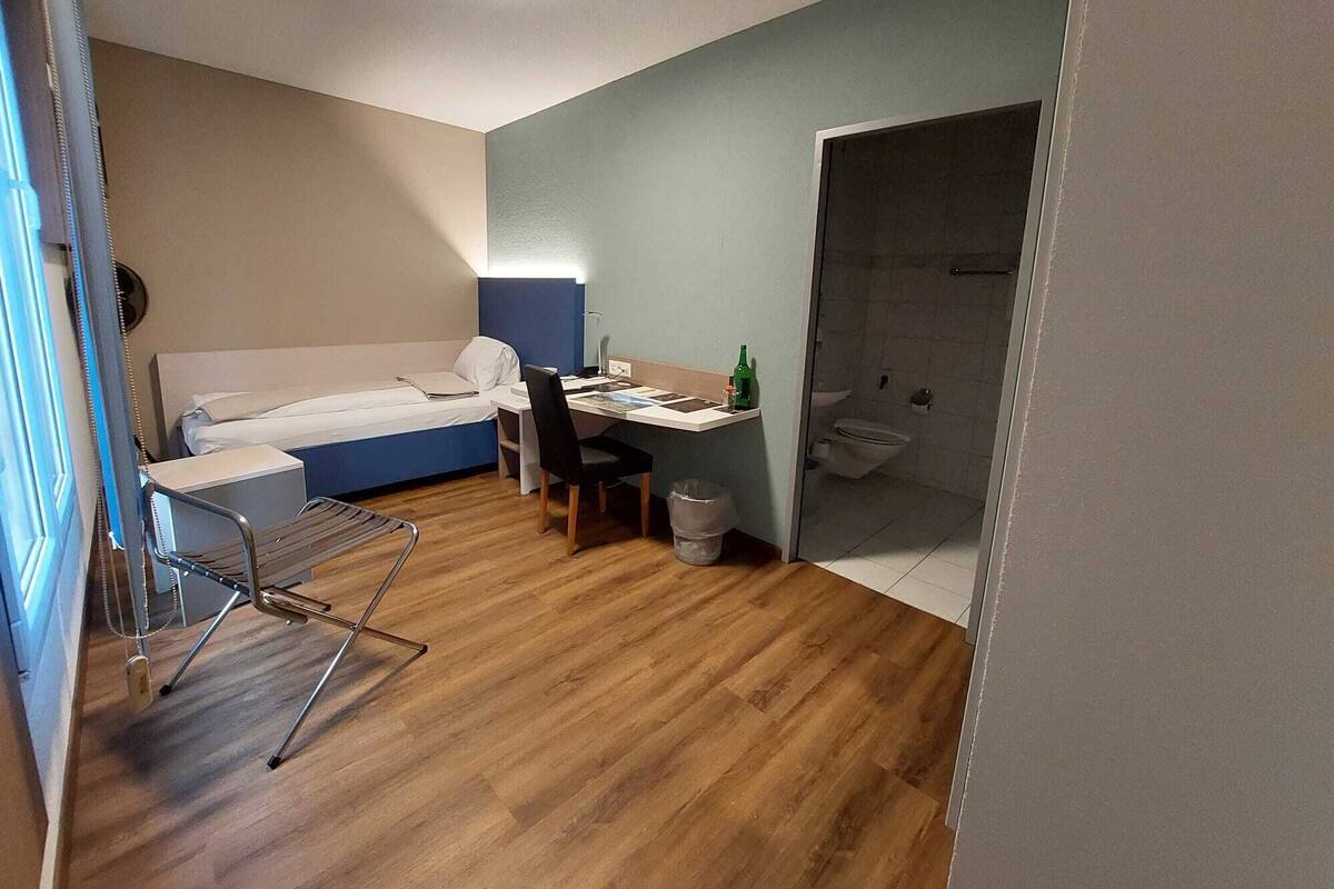 A compact room with a bed, a desk, and a shower area.
