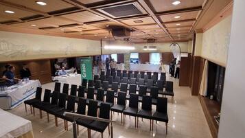 A conference room with rows of chairs, a table with a banner, and a stage area.