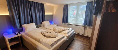 A double bed with a blanket, a bedside table with a lamp, and a window with curtains.