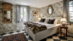 Quarto com piso xadrez, cama com manta de pele, espelho e papel de parede floral.