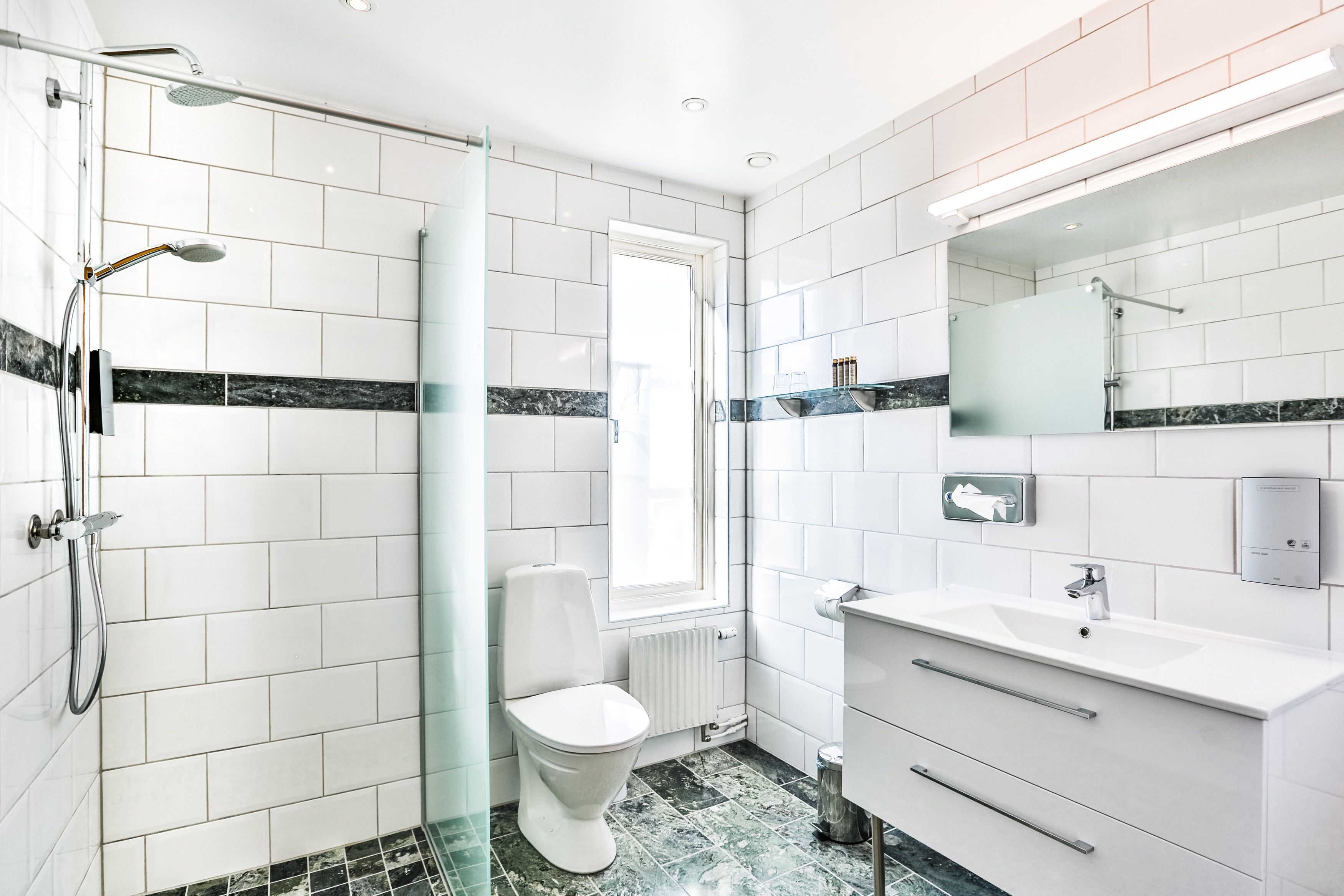 Un baño moderno con azulejos blancos, cabina de ducha de vidrio, inodoro blanco y tocador con espejo.