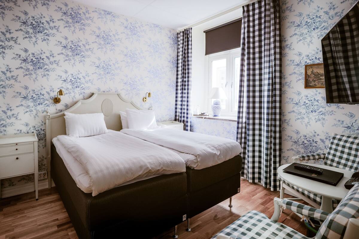 Ein Schlafzimmer mit einem Doppelbett, einem Nachttisch, einem Stuhl, einem Schreibtisch und einem Fenster mit Vorhängen.