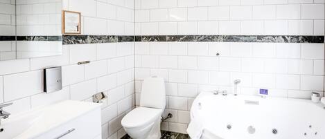 A modern bathroom with white tiles, a marble accent strip, a toilet, a sink, and a bathtub.