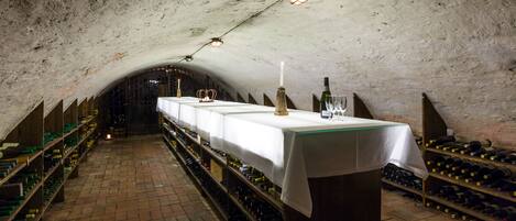 A wine cellar with a long table set for a tasting, surrounded by wine racks.