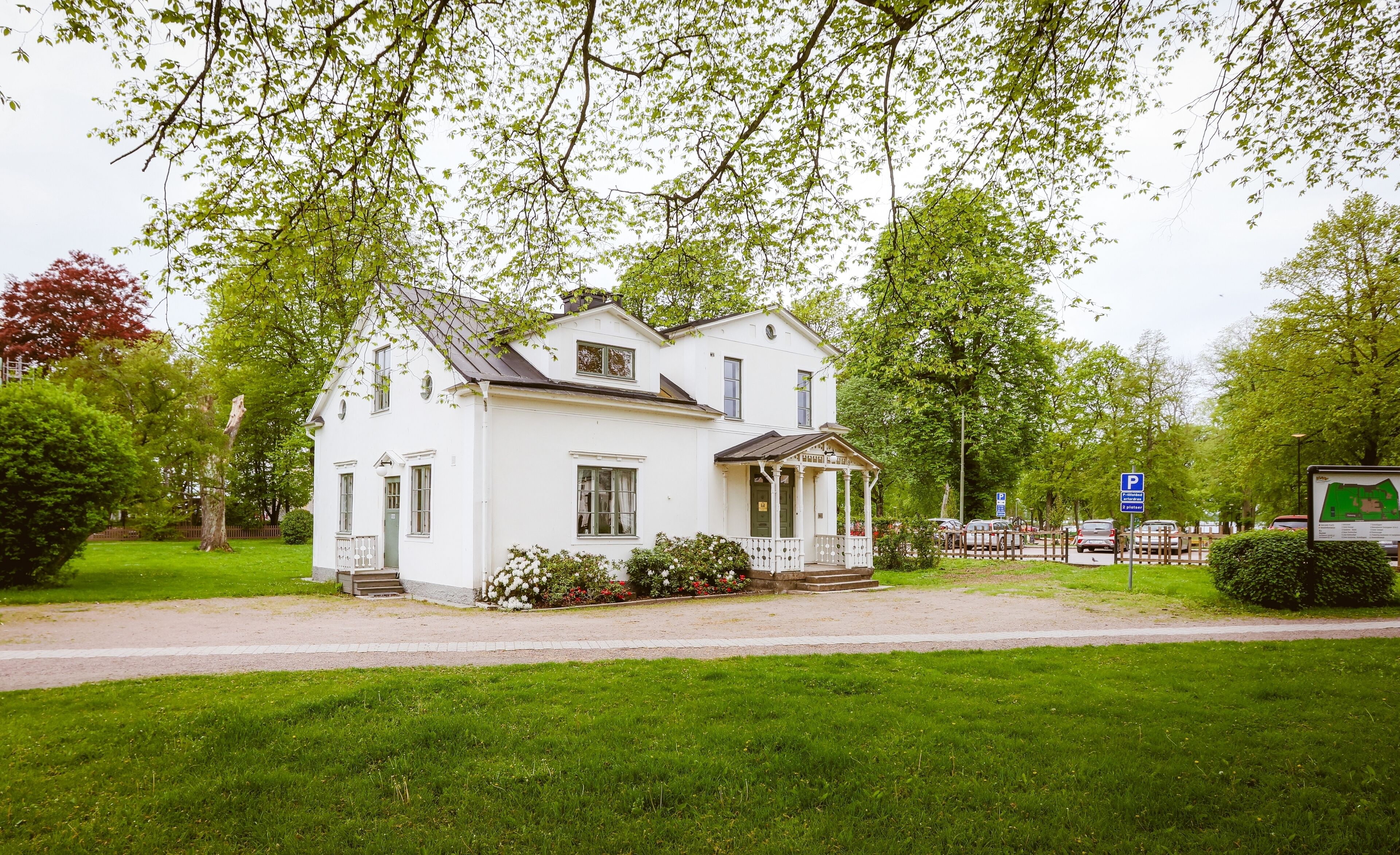 A white two-story house with a porch, surrounded by green grass and trees.