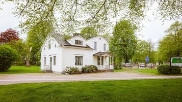 A white two-story house with a porch, surrounded by green grass and trees.