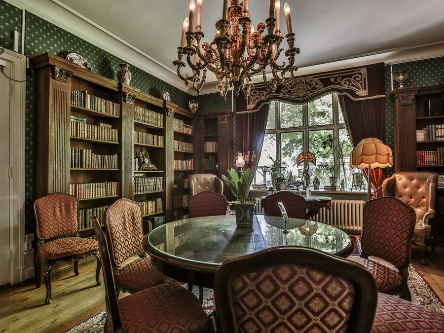 A library with a round glass table, patterned chairs, and a large ornate chandelier.