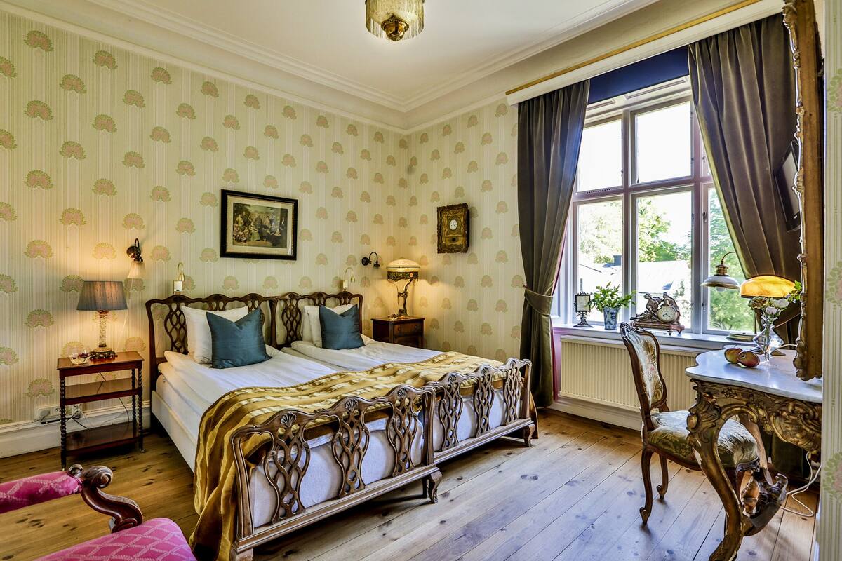 Ein klassisches Schlafzimmer mit einem großen Bett, einem Holzstuhl und einem Fenster mit Vorhängen.