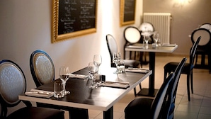 A dining area with tables set for two, chairs, and a wall-mounted menu board. - Logis Hôtel Le Chene Dore (La Loupe)