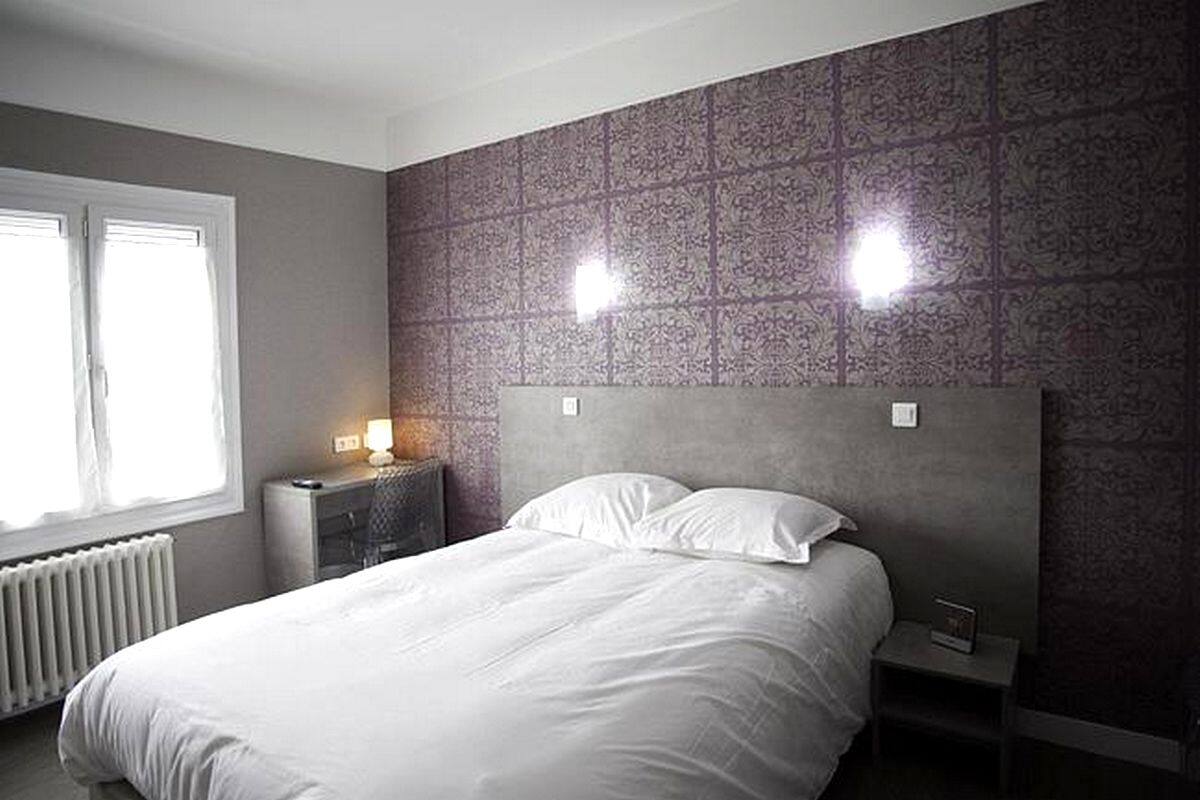 A bedroom with a large bed, a nightstand, and a wall-mounted light fixture.