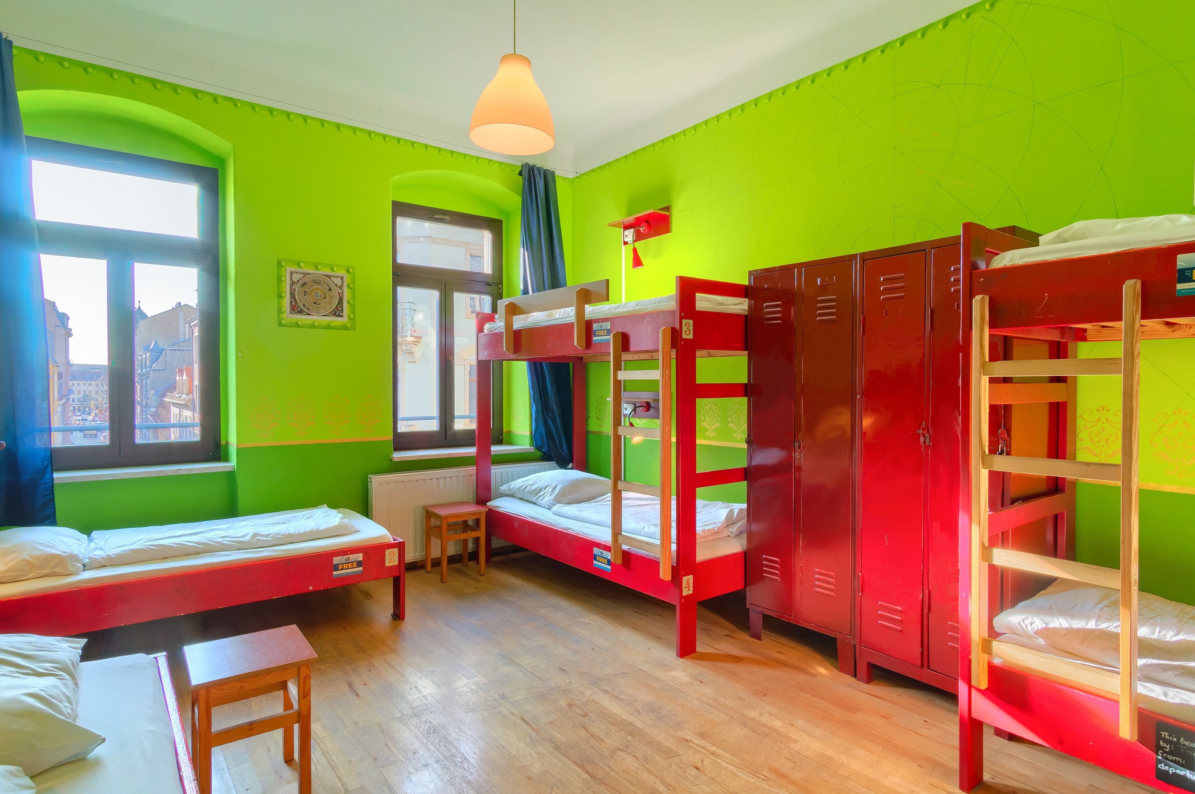 A dormitory room with bunk beds, a small table, and a window with a view of buildings outside.