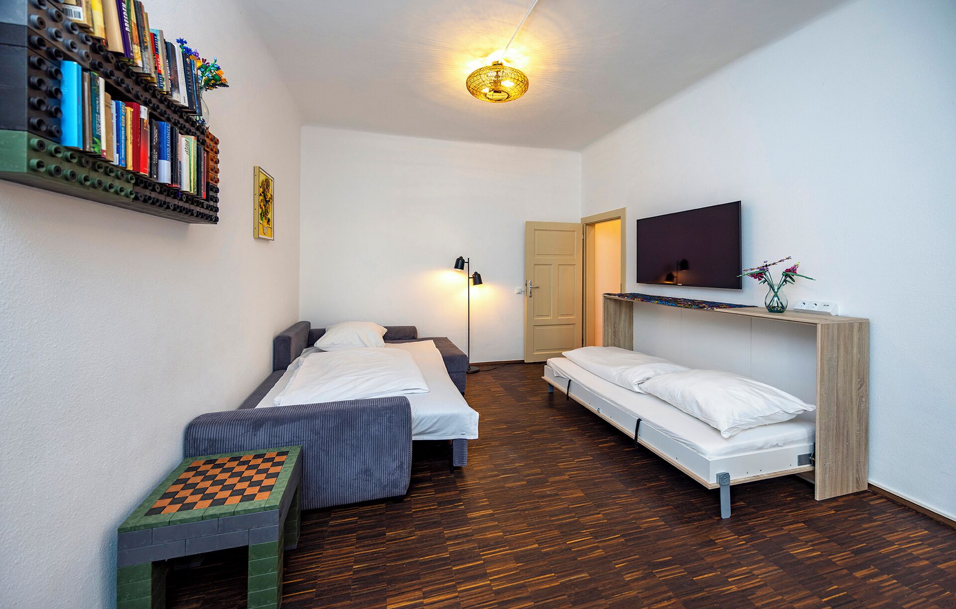 Une chambre avec deux lits, une télévision, une bibliothèque et une petite table.