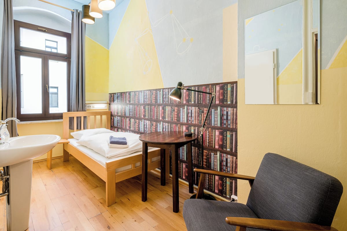 A room with a bed, a desk, a chair, a bookshelf, and a window.